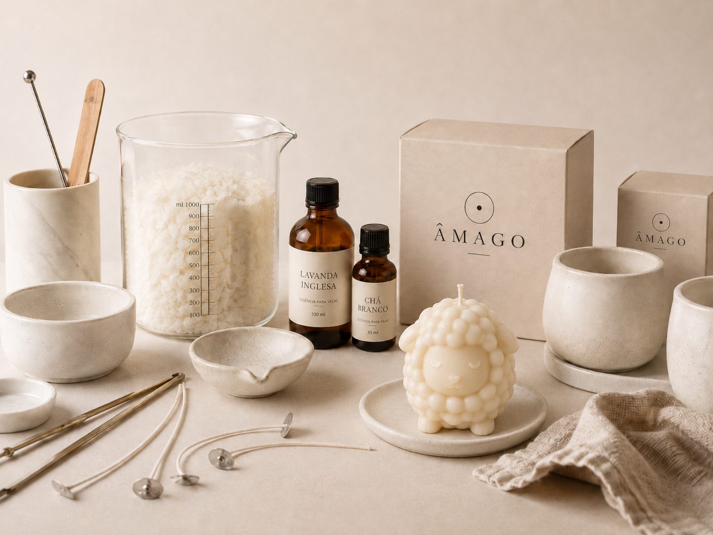 Bancada de produção da ÂMAGO — cera em flocos, essências de Lavanda Inglesa e Chá Branco, recipientes e a vela Ovelhinha